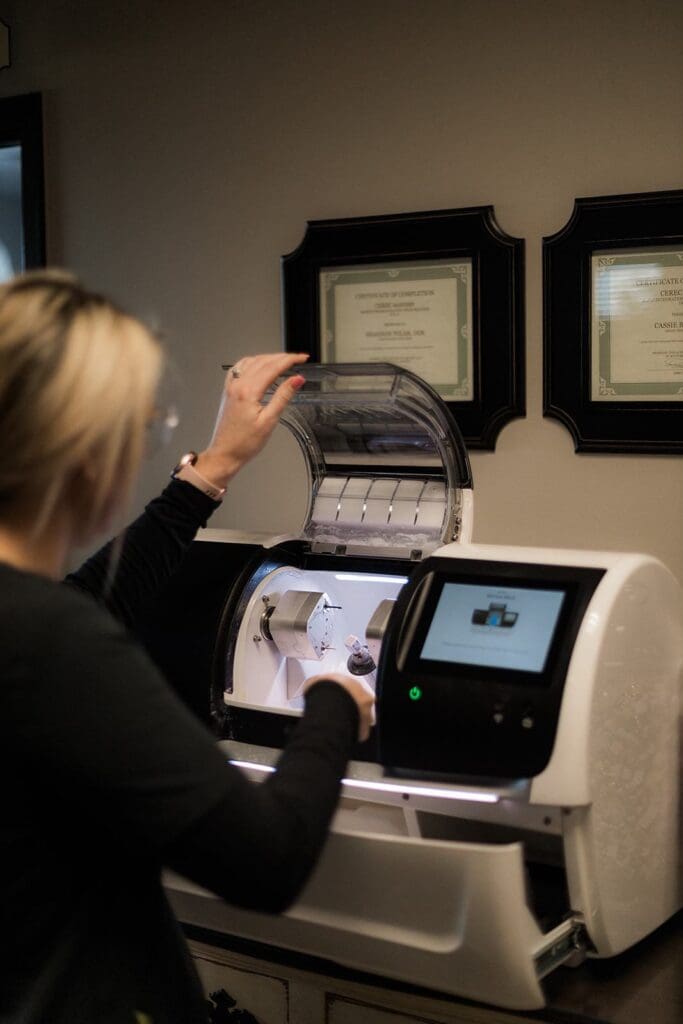 At Origin Dental Wellness, your holistic, health-centered dentist in Tulsa, Oklahoma, a team member skillfully manages a dental milling machine under the guidance of two proudly displayed certificates. We combine advanced technology with a natural approach to ensure our patients receive top-tier dental care that aligns with their overall well-being.